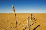 outback australian drought with fence across barren treeless plains and rain gauge on post
